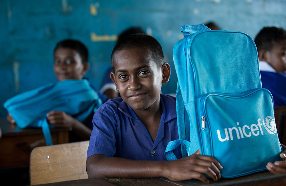 A boy smiles at his desk with a UNICEF school bag © UNICEF/UN0410101/Stephen/Infinity Images