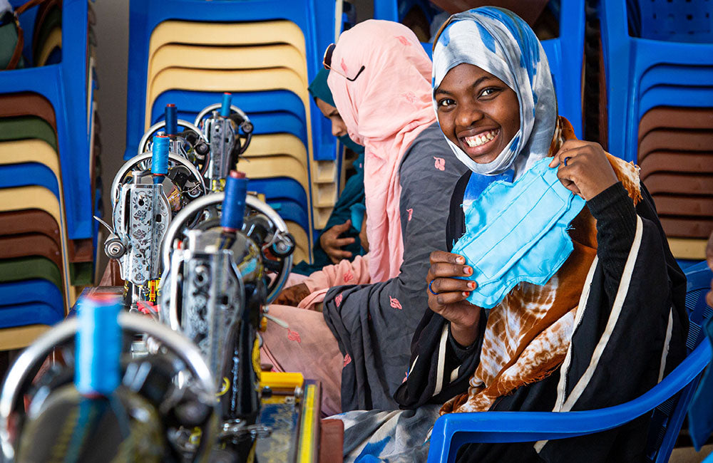 A girl smiles and shows a feminine hygiene pad that she has made with a sewing machine. © UNICEF/UN0467618/Pouget