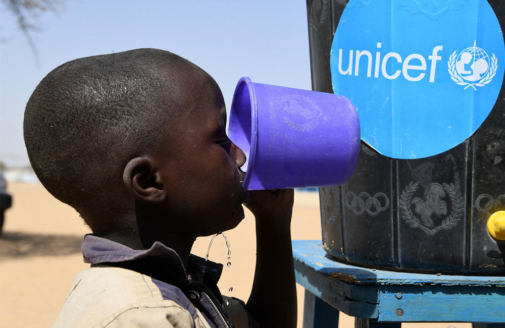 A child drinks water from a UNICEF water tank. © UNICEF/UN0594579/Dejongh