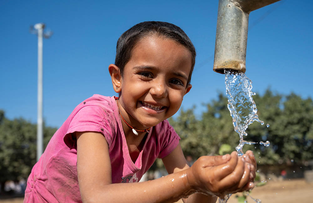 A child smiles while drinking water from a tank. © UNICEF/UN0389282/Panjwani
