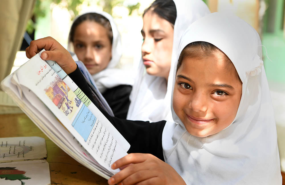 Children smile while reading from a school book. © UNICEF/UN0340026/Frank Dejongh