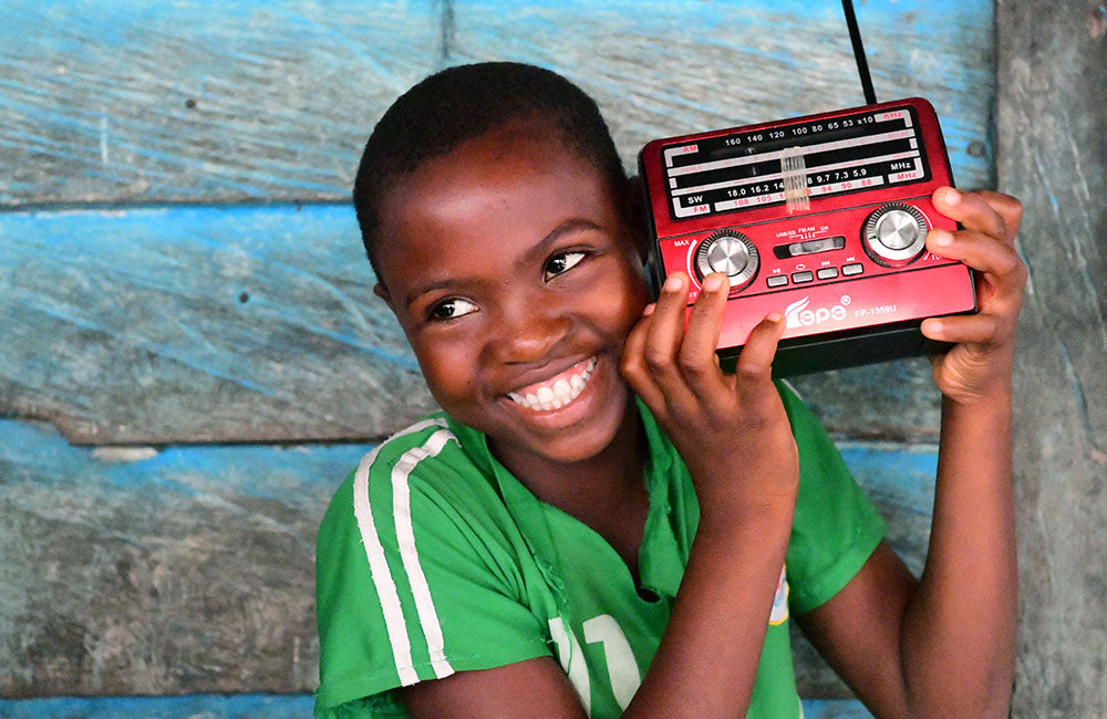 A child smiles while listening to a portable radio. © UNICEF/UN0419385/Dejongh